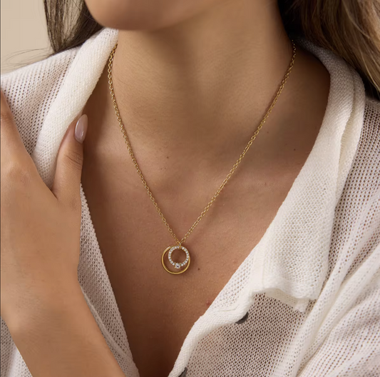 Close up of a gold necklace with circular pendant being worn