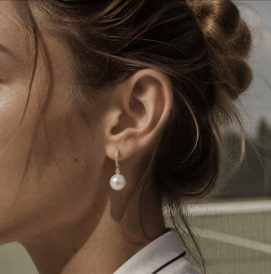 A close-up side profile of a woman wearing a single drop earring with a white pearl and a small gold-toned setting.