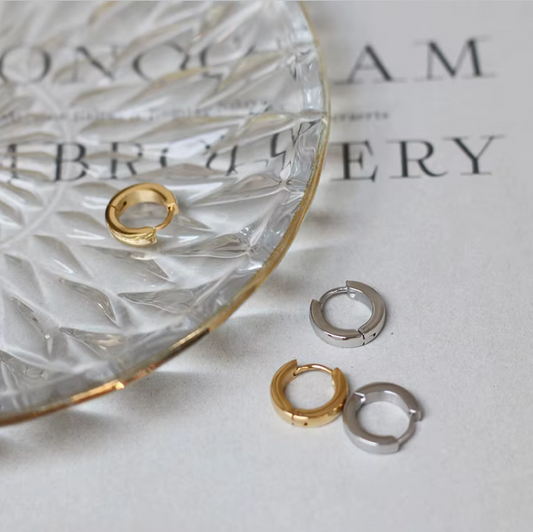 Gold and silver hoop earrings on a textured surface with a glass dish.