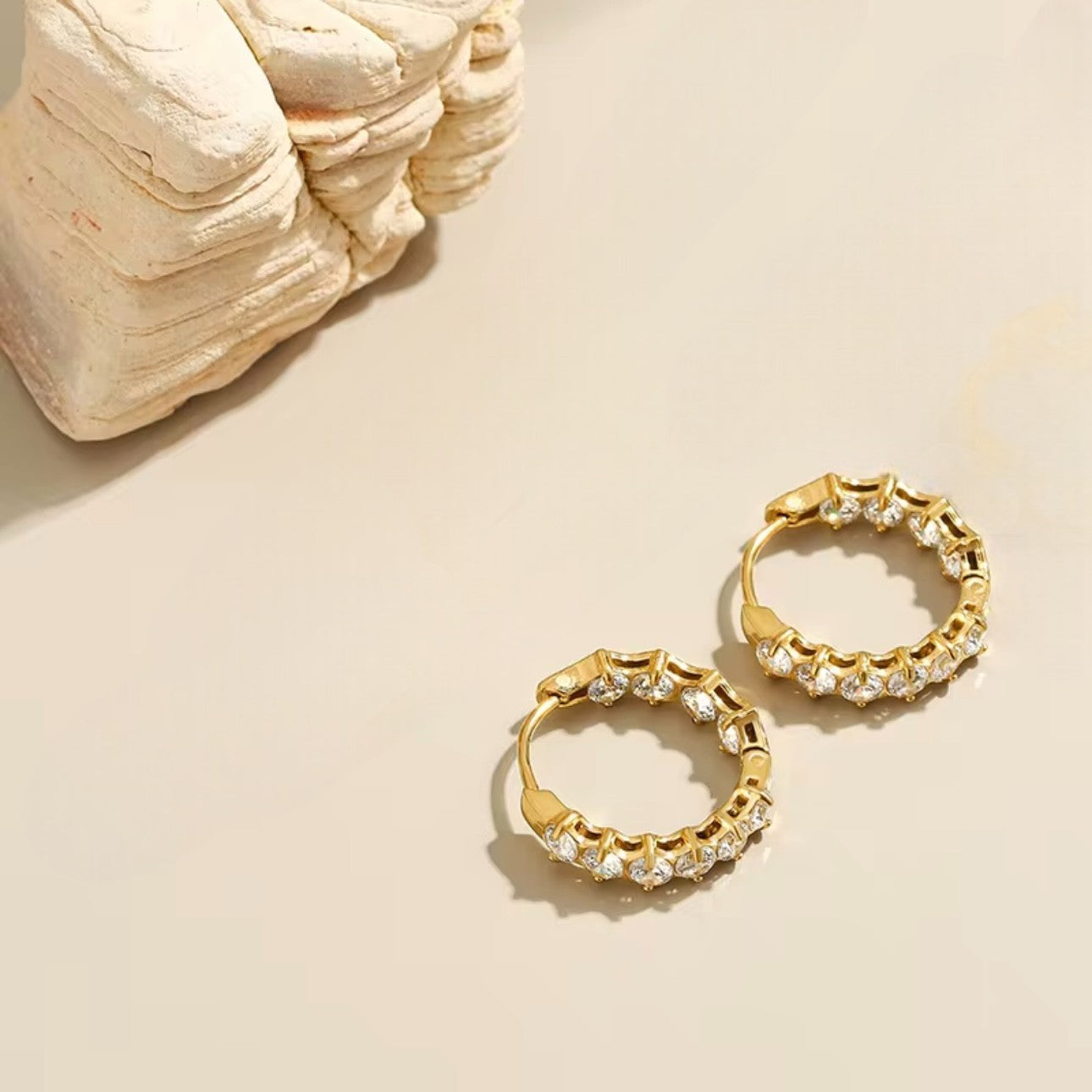 Gold hoop earrings with clear stones on a beige surface