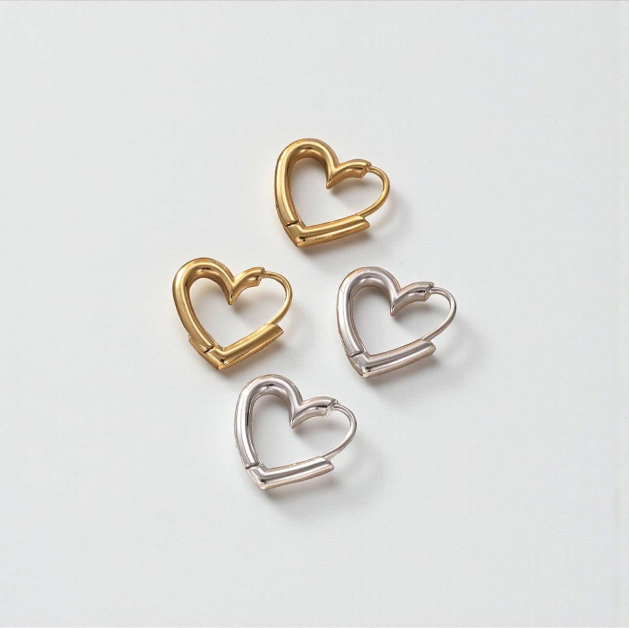 Two pairs of heart shaped hooped earrings. One gold and one silver. Pictured on a white background