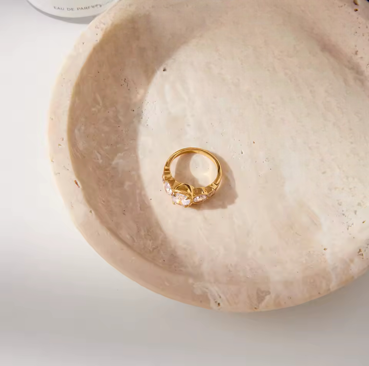 Gold ring with clear stones on a beige stone surface