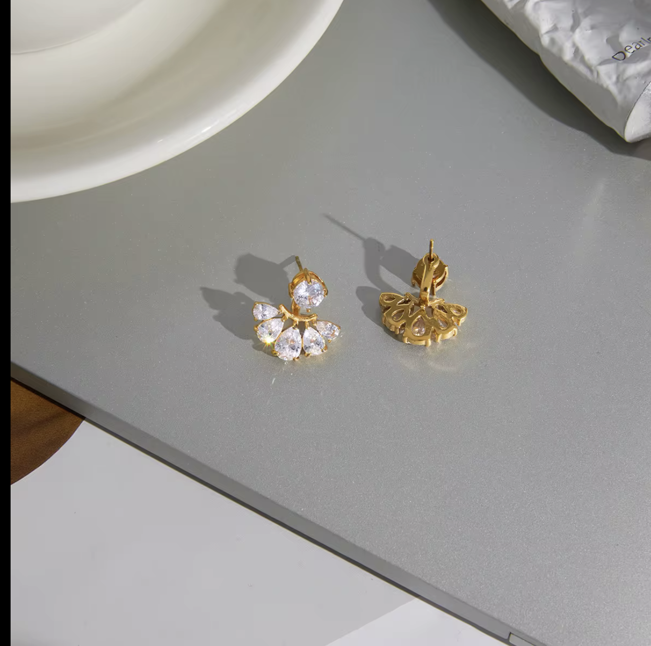 gold earrings with clear pear shaped gemstones pictured on a grey background