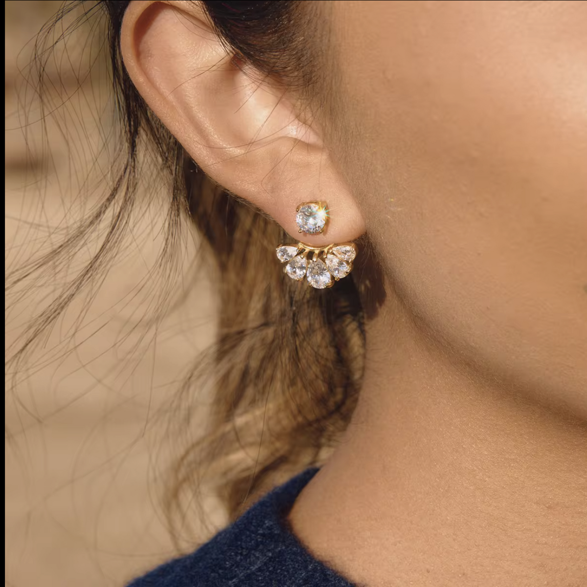 gold earrings with clear pear shaped gemstones pictured being worn in the ear