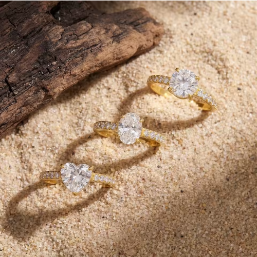 Two gold and diamond rings on a sandy surface with a wooden log in the background.