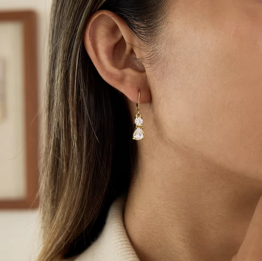 Close-up of a person wearing a gold earring with three clear stones.