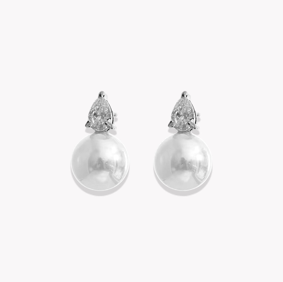 A pair of silver stud earrings featuring a pear-cut clear gemstone in a prong setting above a large, lustrous white pearl drop, shown on a light gray background.