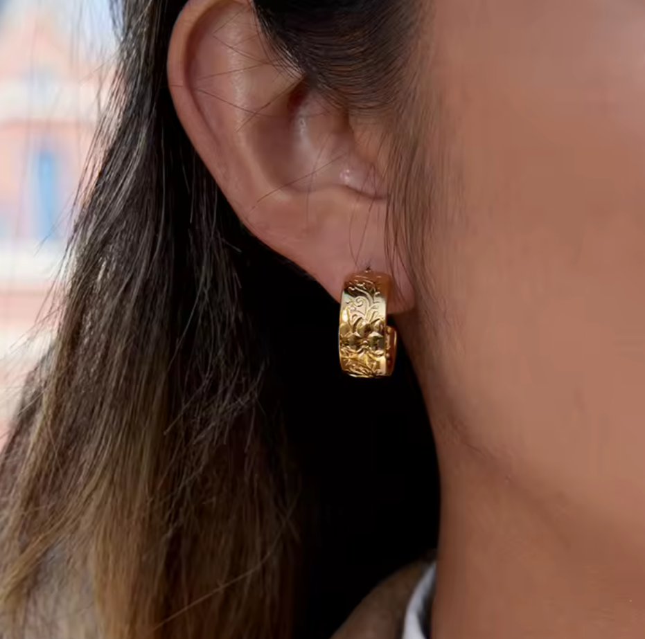 Gold earrings featuring intricate embossed detail being worn in an ear