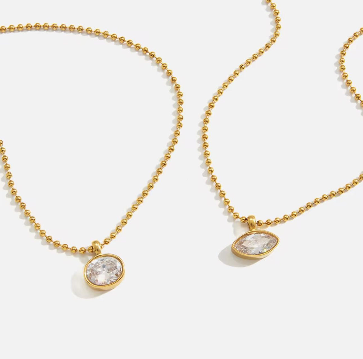 Two gold ball-chain necklaces with oval bezel-set clear gemstones, displayed on a clean white background.
