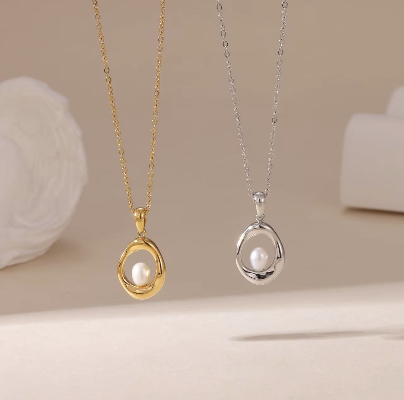 gold and silver necklaces, both with circular pendant featuring a small pearl inside pictured on a neutral background