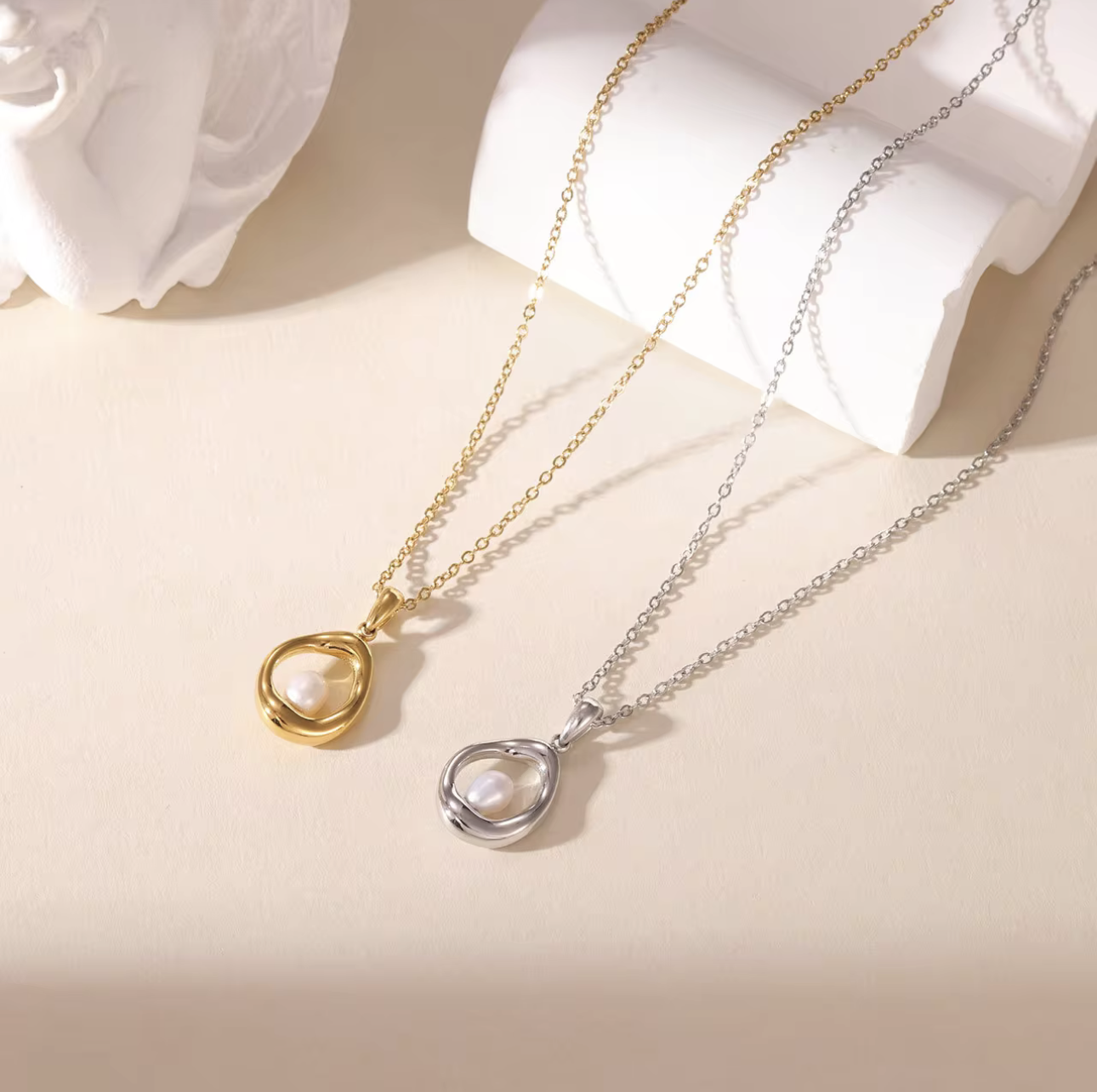gold and silver necklaces, both with circular pendant featuring a small pearl inside pictured on a neutral background