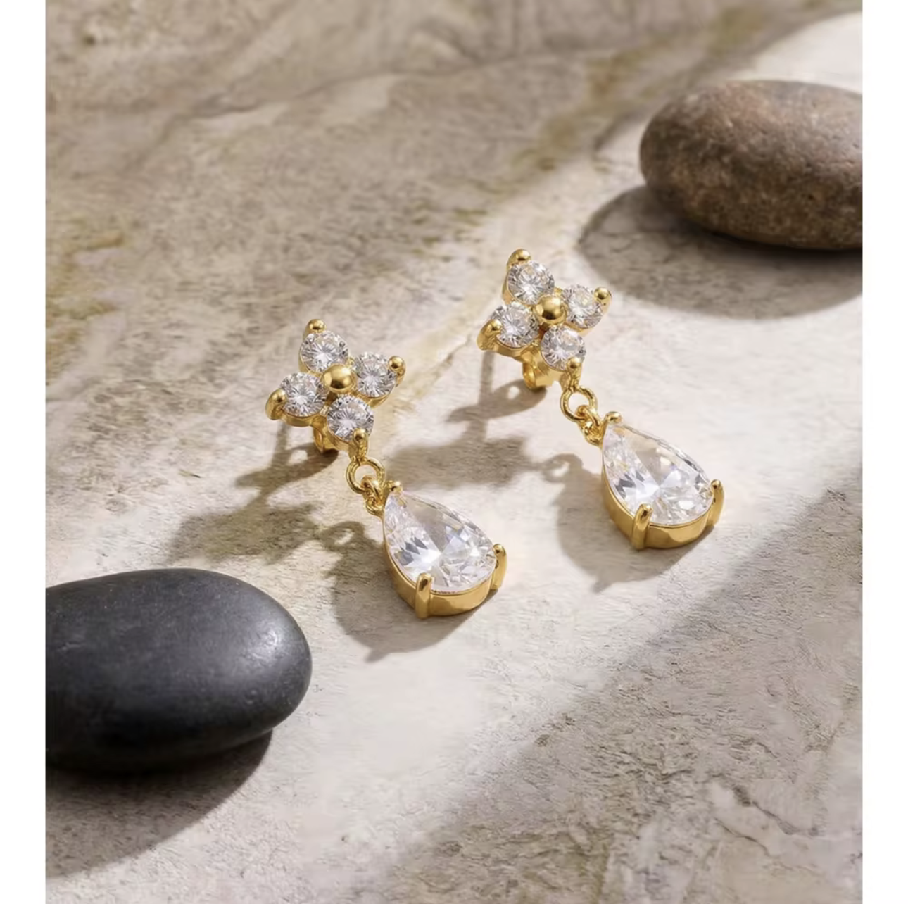 Gold earrings with clear teardrop-shaped gemstones on a stone surface