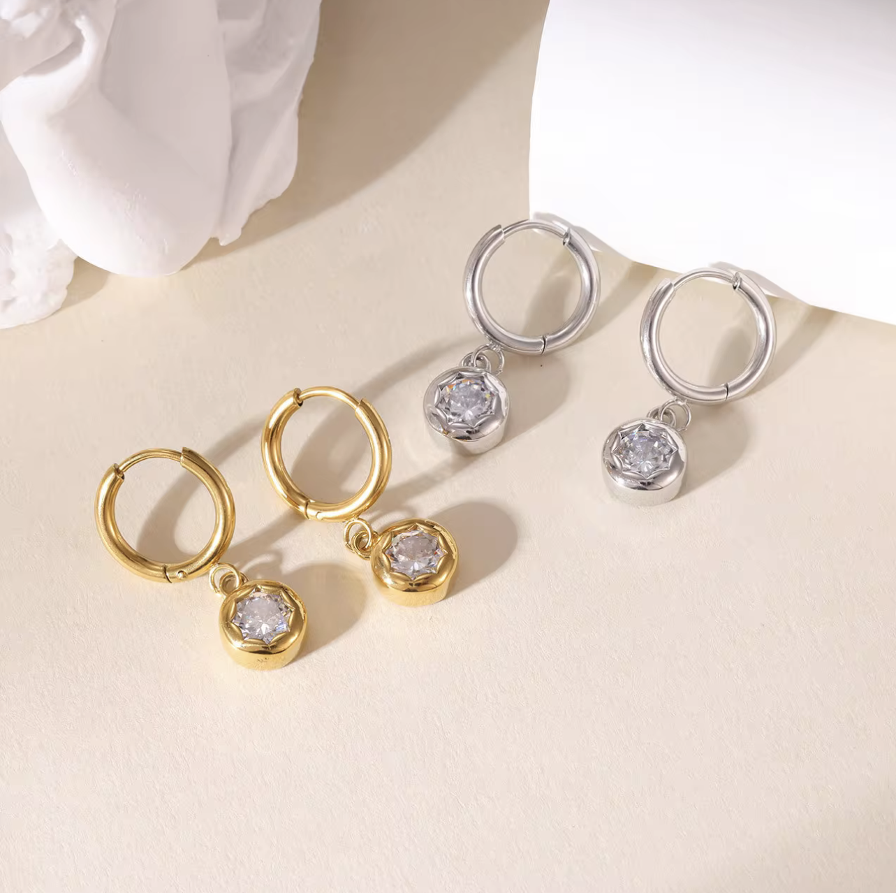 gold and silver hooped earrings with bezel set drop gemstone pictured on a light beige background