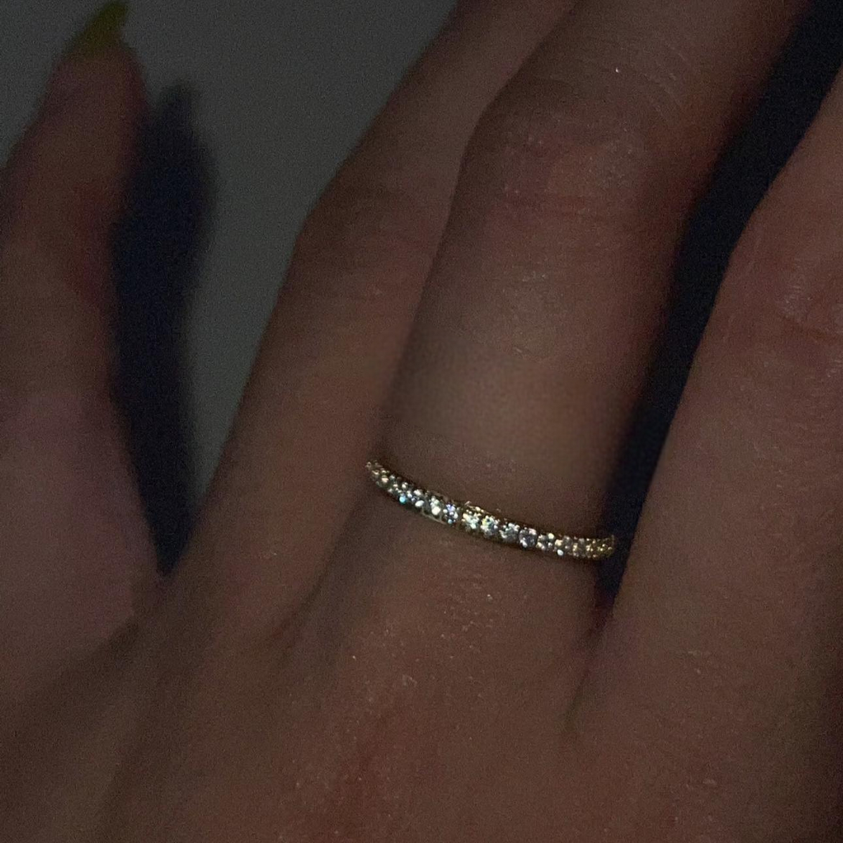 Gold ring with small diamonds on a finger against a dark background