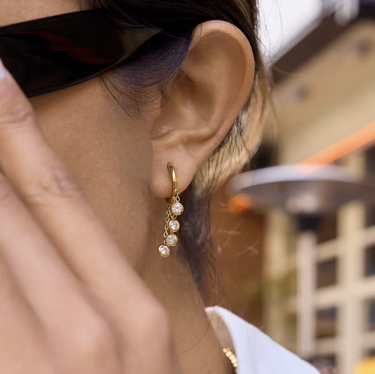 Close-up of a person wearing gold hoop earrings with clear gemstones, blurred background