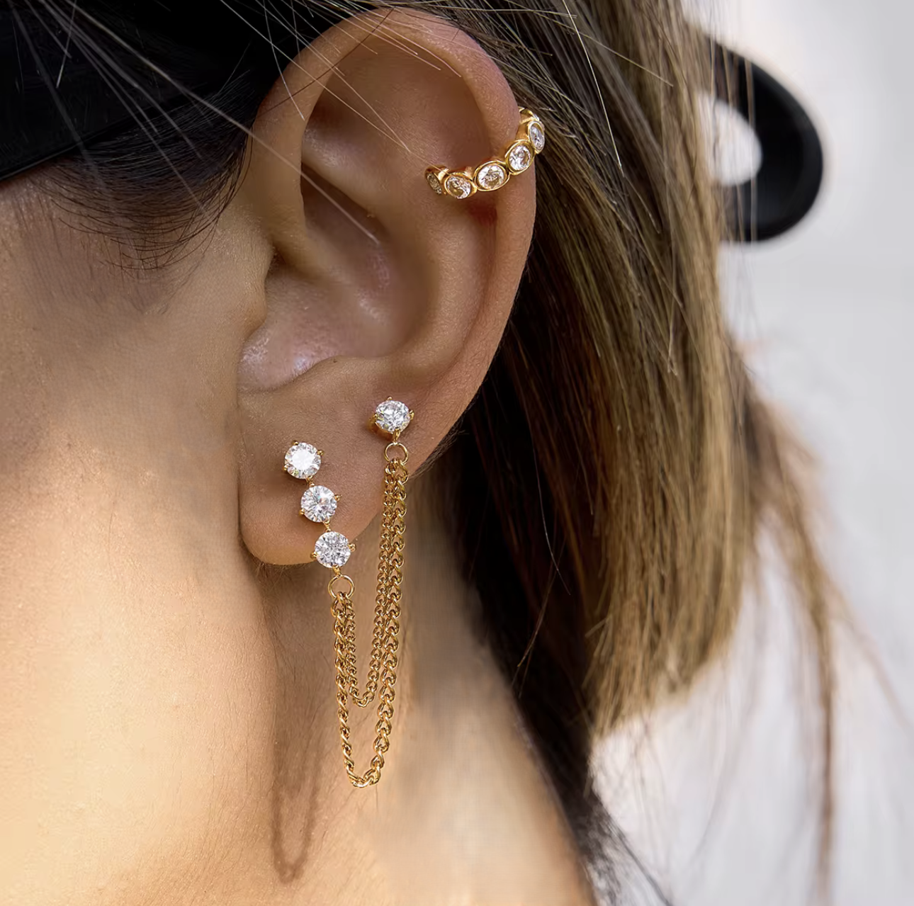 Close up of gold earrings with a dangly chain being worn in an ear