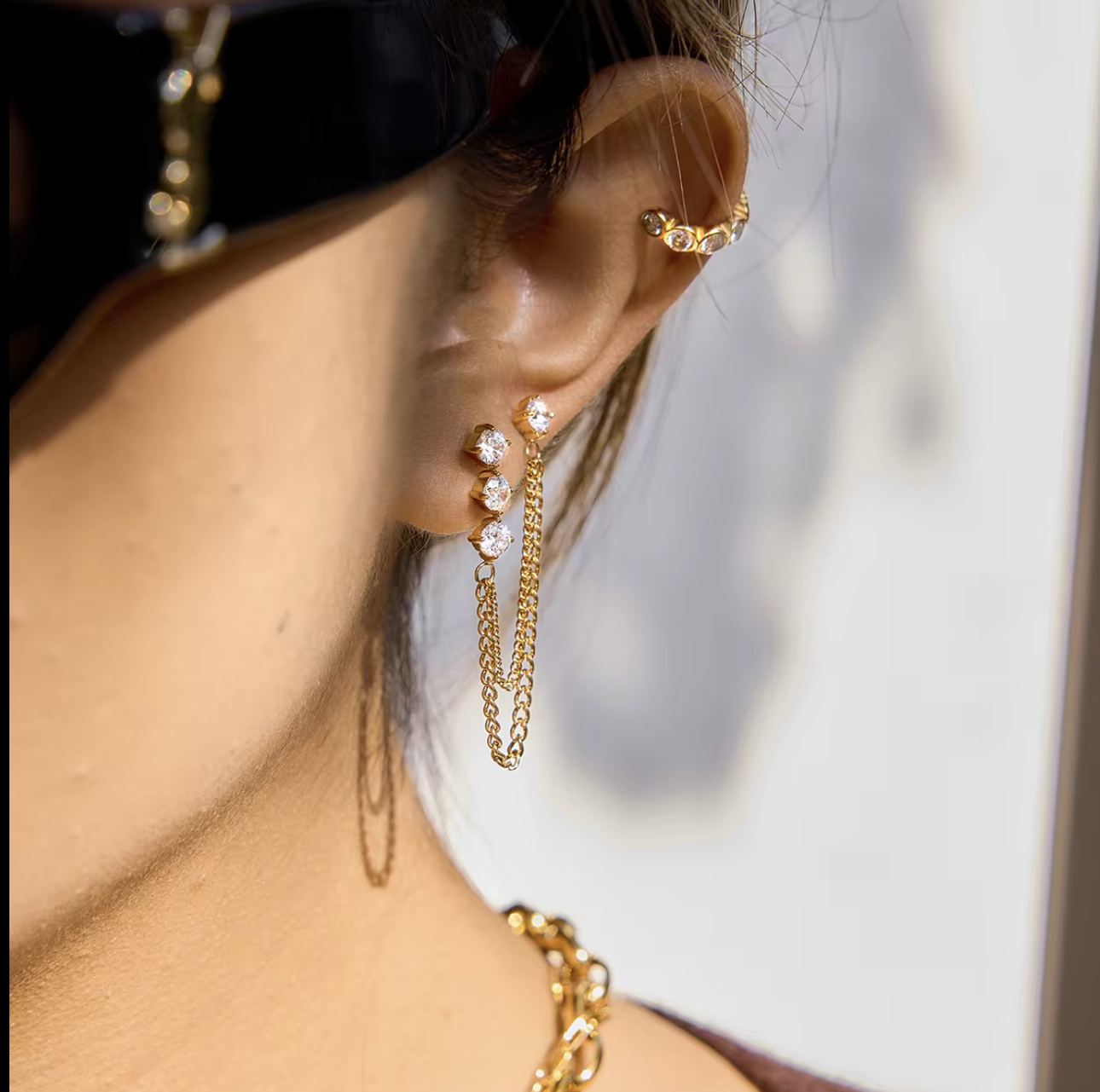 Close up of gold earrings with a dangly chain being worn in an ear