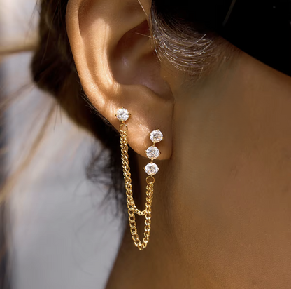 Close up of gold earrings with a dangly chain being worn in an ear