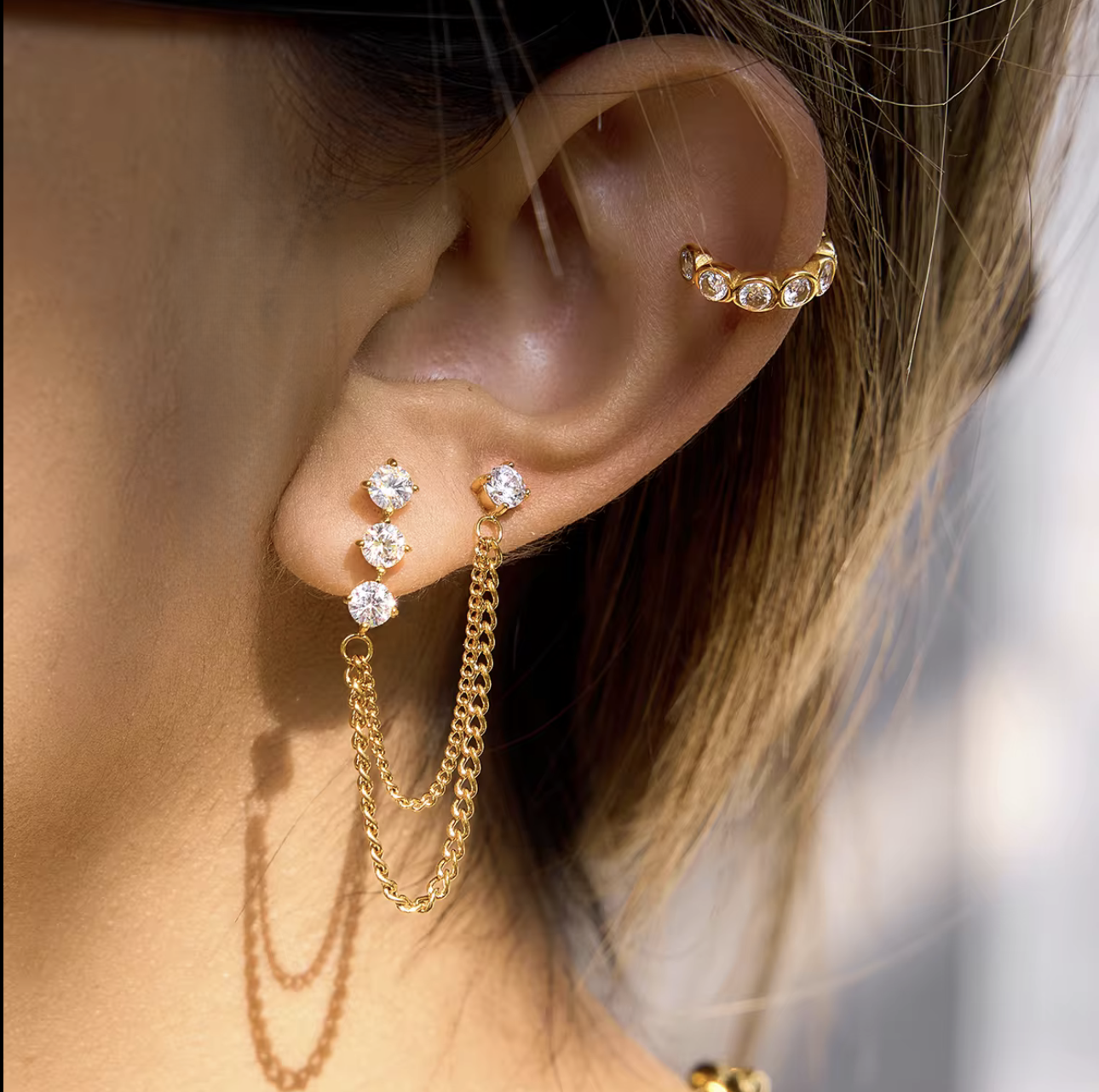 Close up of gold earrings with a dangly chain being worn in an ear