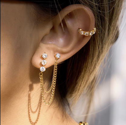 Close up of gold earrings with a dangly chain being worn in an ear