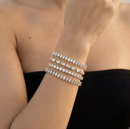 A close-up of a person's wrist wearing four stacked diamond tennis bracelets in silver and yellow gold tones, set against a black top and soft skin tones.