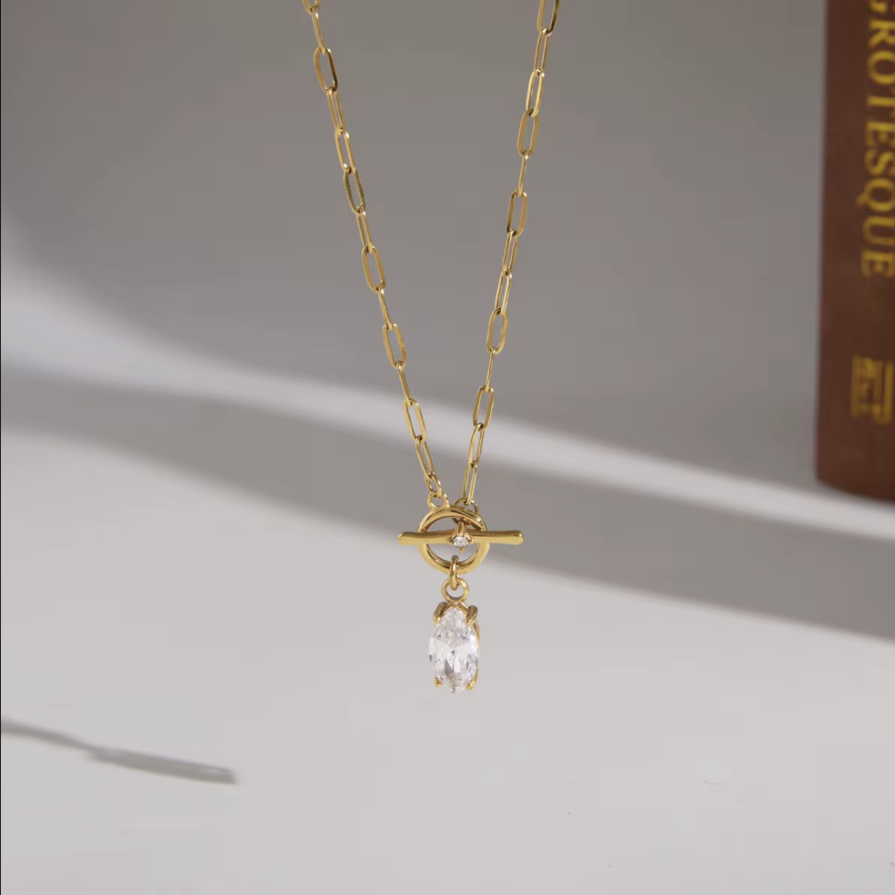 gold necklace with marquise gemstone pendant pictured hanging with a grey background