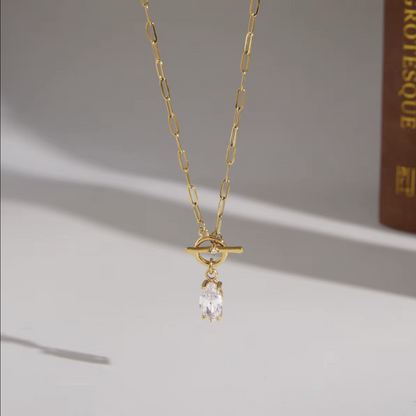 gold necklace with marquise gemstone pendant pictured hanging with a grey background