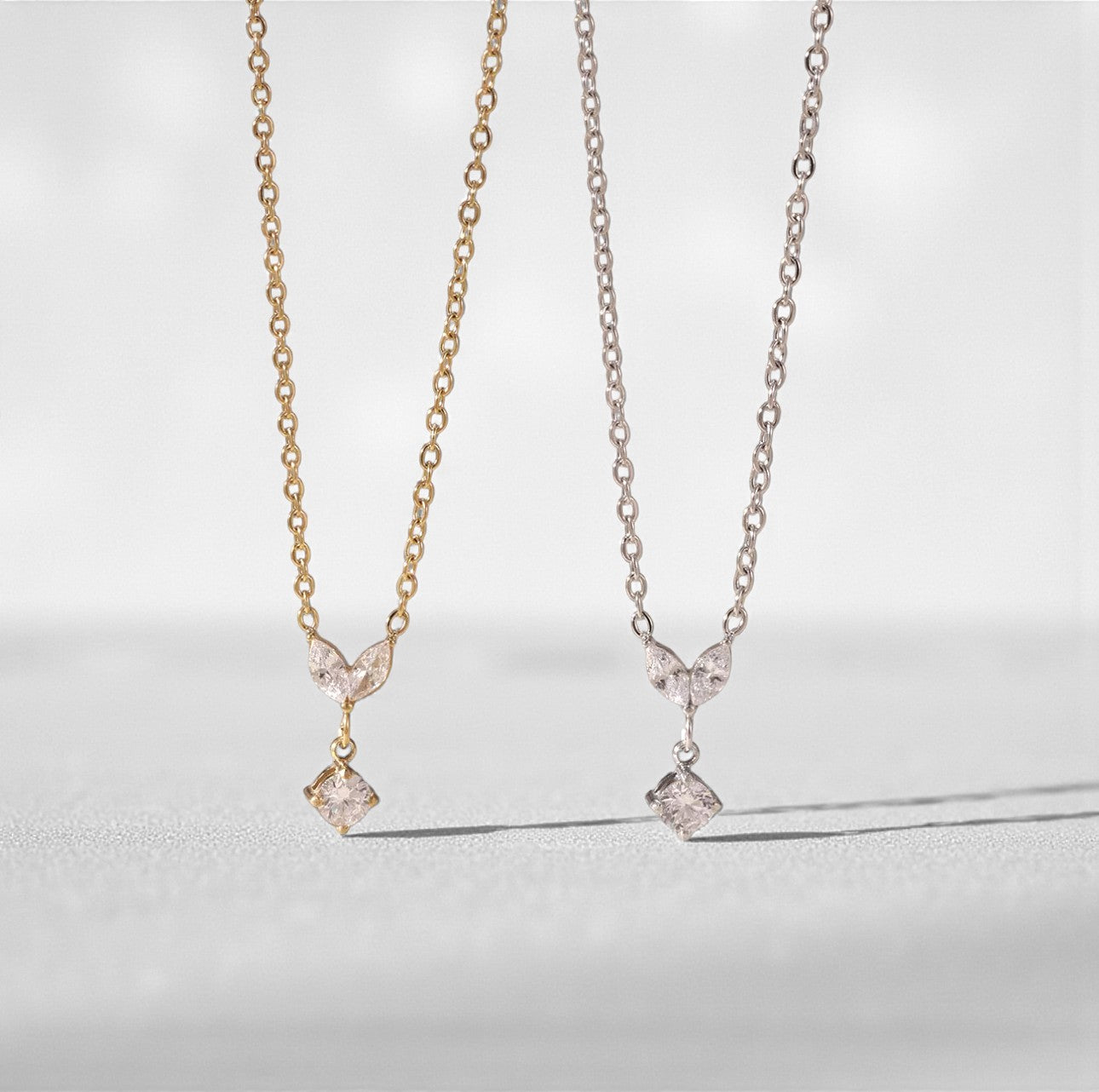 Two necklaces, one gold and one silver. Both with a small marquise and round gemstone pendant on a light grey background