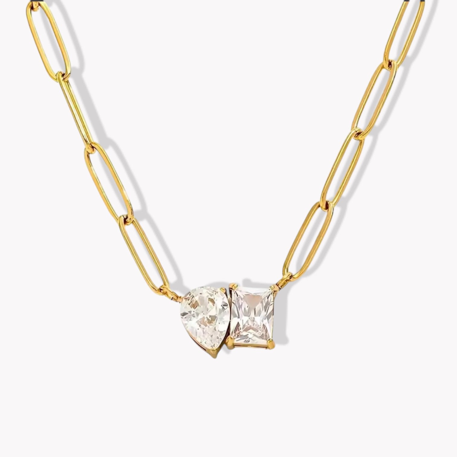 Paperclip chain necklace with a clear stons pendant made of a pear shape and emerald cut gemstone presented together. Pictured on a light grey background