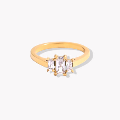 Gold ring with three emerald-cut diamonds. The centre gemstone is larger than the other two either side, which are slightly smaller. Pictured on a white background