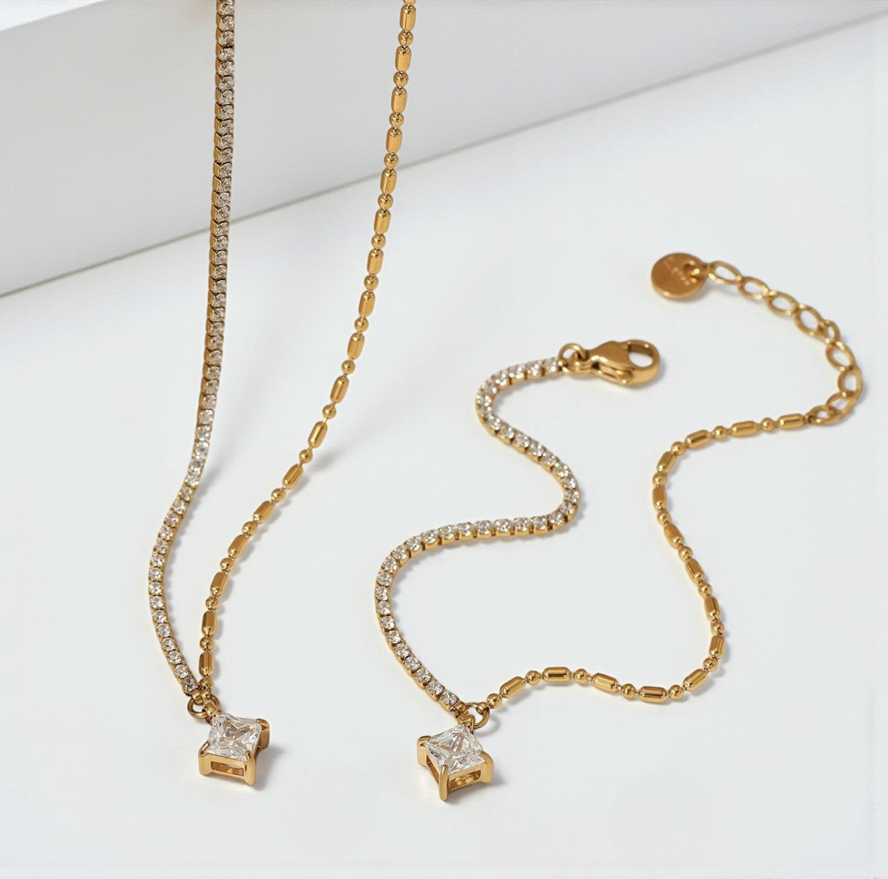 Gold necklace and bracelet both with a square cut gemstone charm, arranged next to each other
