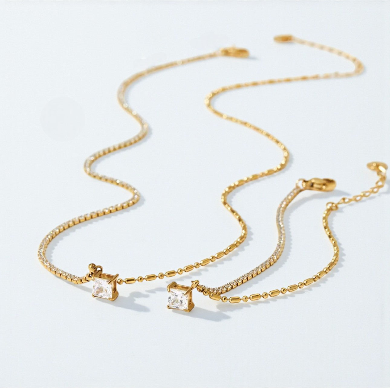 Gold chain necklace and bracelet with clear gemstones on a light gray background