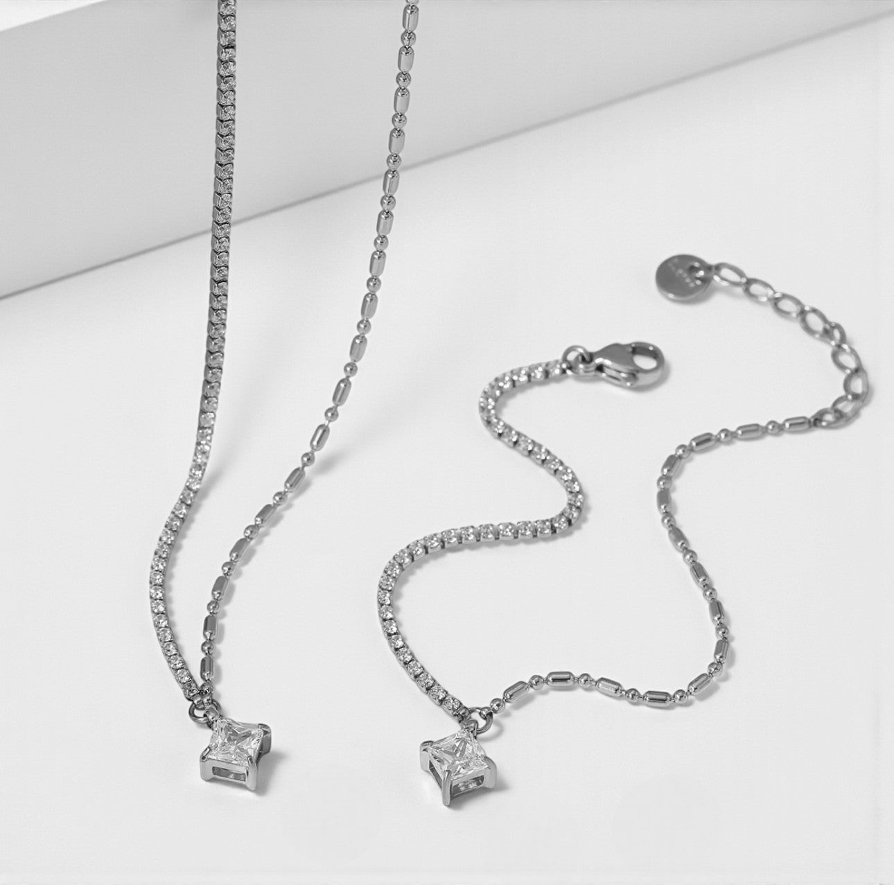 Silver bracelet and necklace both with a princess cut gemstone on a white background