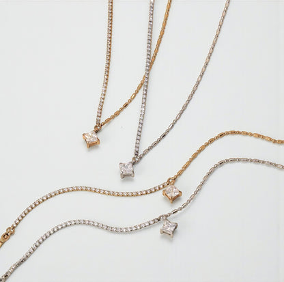 Silver and gold bracelet with a princess cut gemstone on a white background. Matching necklaces are laid next to the bracelets