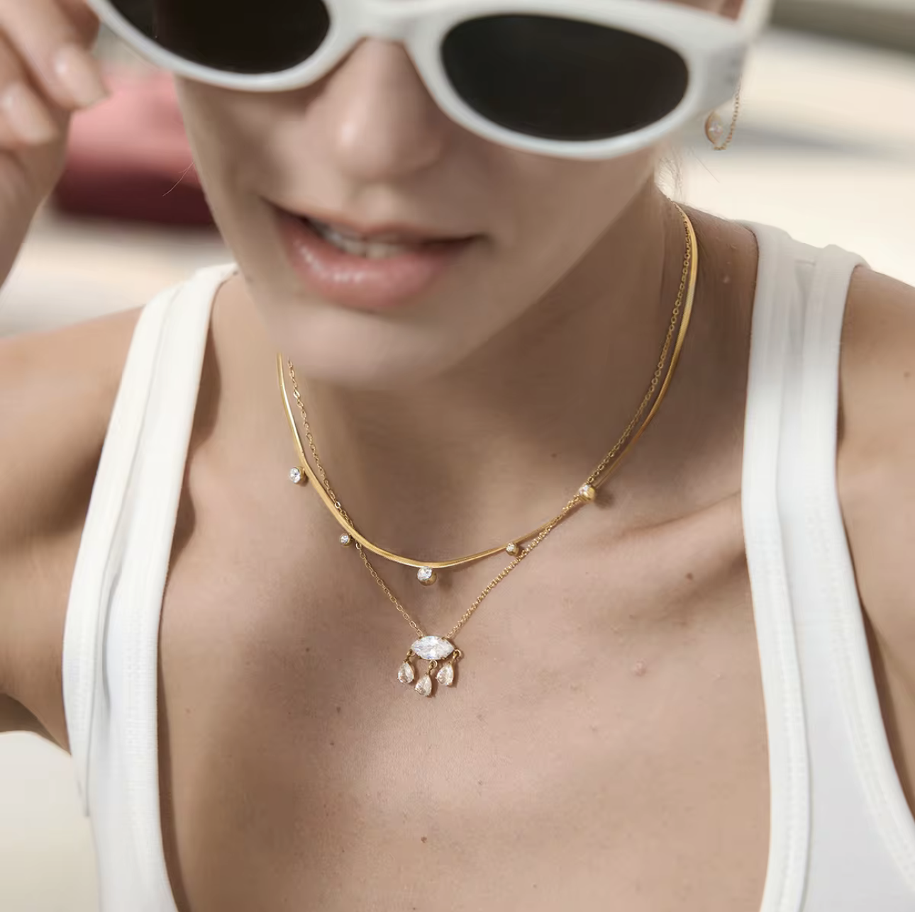 Close-up of a person wearing a gold necklace with a pendant, with sunglasses partially covering the face.