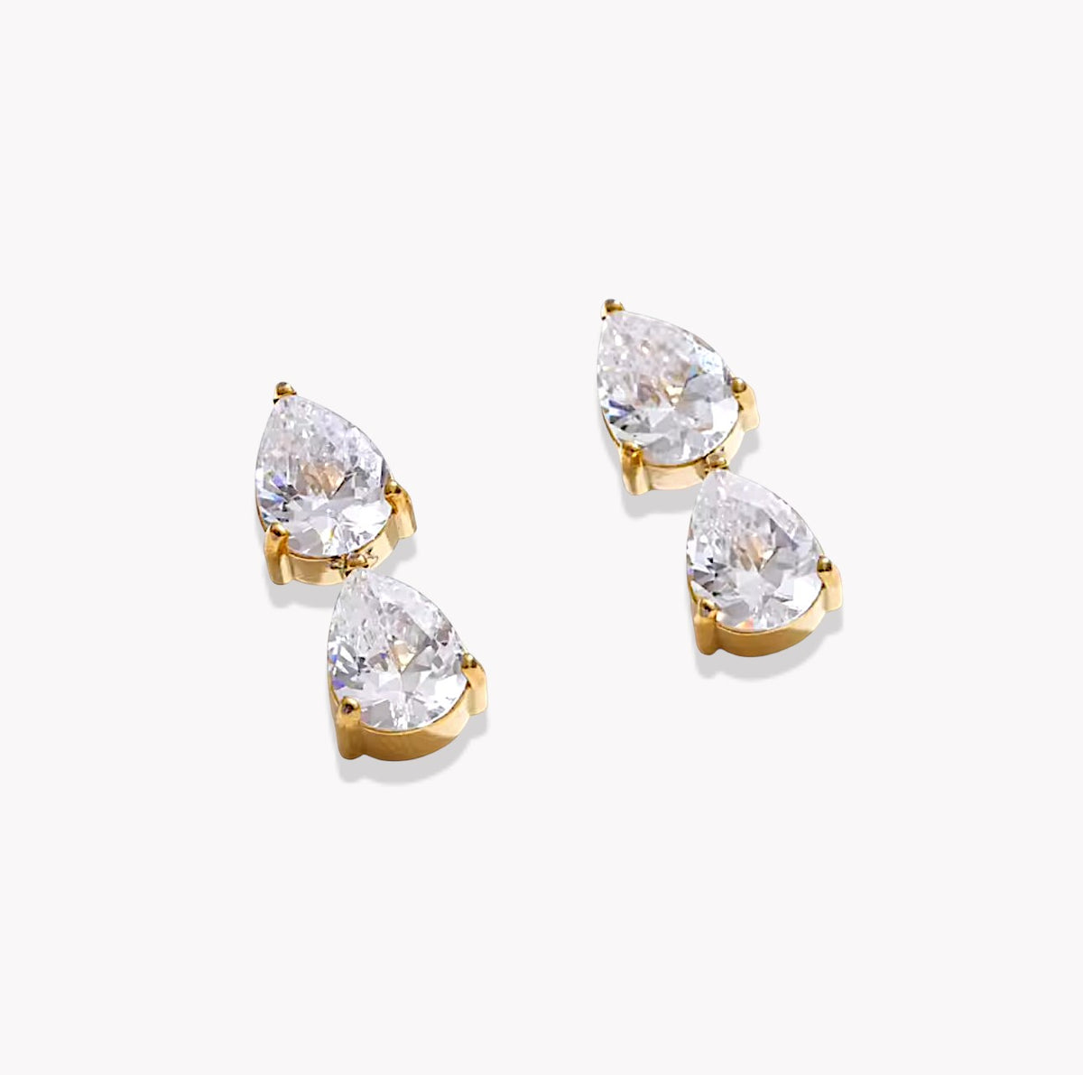Four pear-cut clear gemstones in gold prong settings, arranged in two pairs on a clean white background.