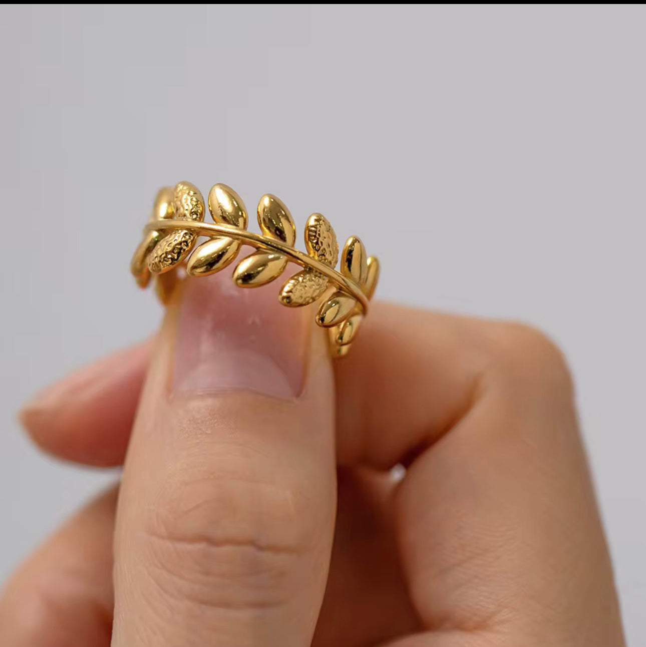 An 18k gold ring with leaf sculpted details around the band, displayed on a finger
