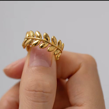 An 18k gold ring with leaf sculpted details around the band, displayed on a finger
