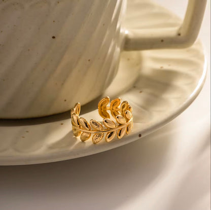 An 18k gold ring with leaf sculpted details around the band, displayed on a neutral background