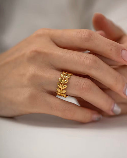 An 18k gold ring with leaf sculpted details around the band, displayed on a finger