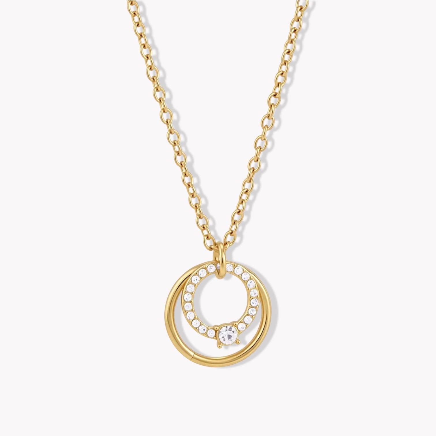 Close up of a gold necklace with circular pendant on a light coloured background