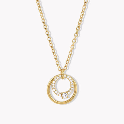 Close up of a gold necklace with circular pendant on a light coloured background