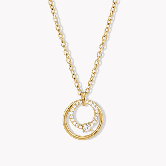 Close up of a gold necklace with circular pendant on a light coloured background