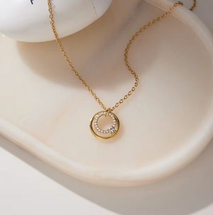 Close up of a gold necklace with circular pendant on a light coloured background