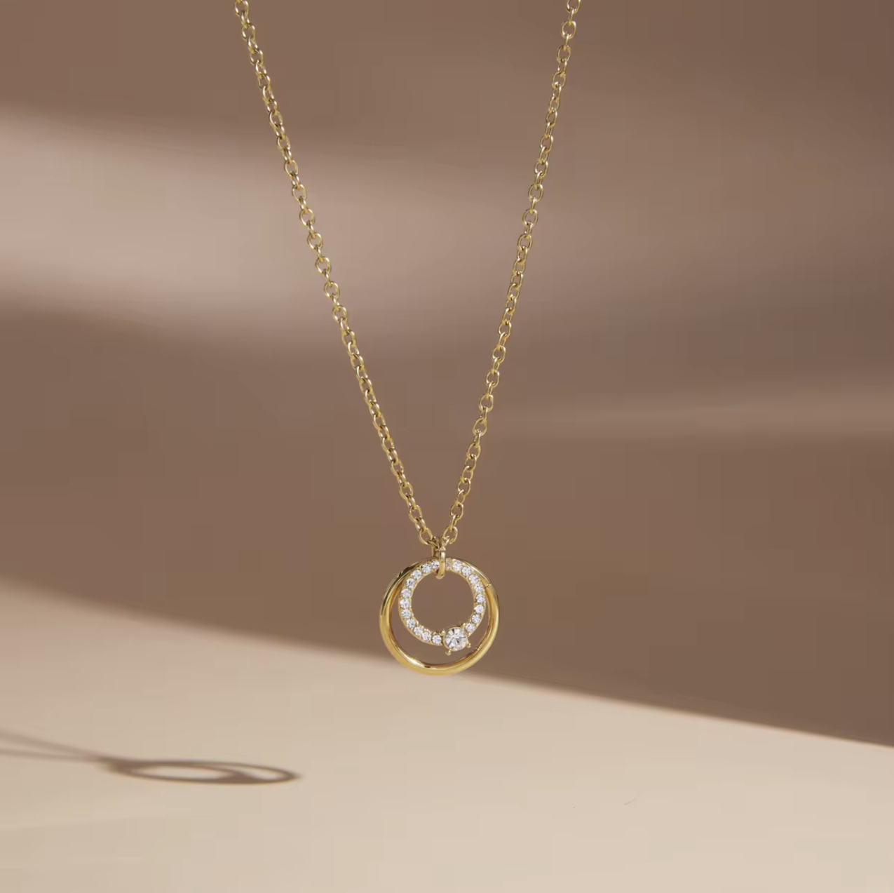 Close up of a gold necklace with circular pendant on a light coloured background