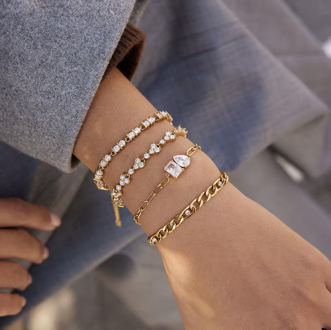 two gold bracelets with clear gemstones pictured together on a wrist