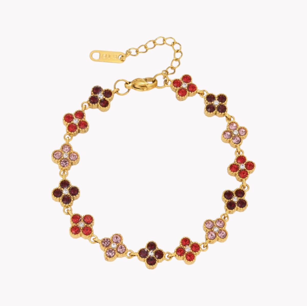 A gold-tone floral bracelet with alternating red, dark brown, and light pink rhinestone clover motifs, shown on a plain white background.