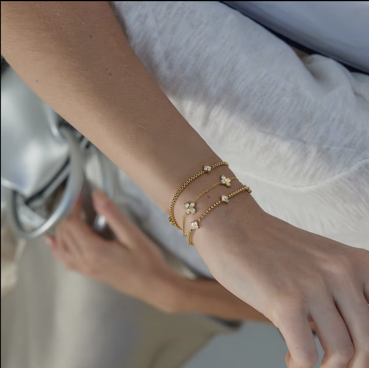 Close-up of a wrist wearing gold bracelets with small flowers, against a blurred background.