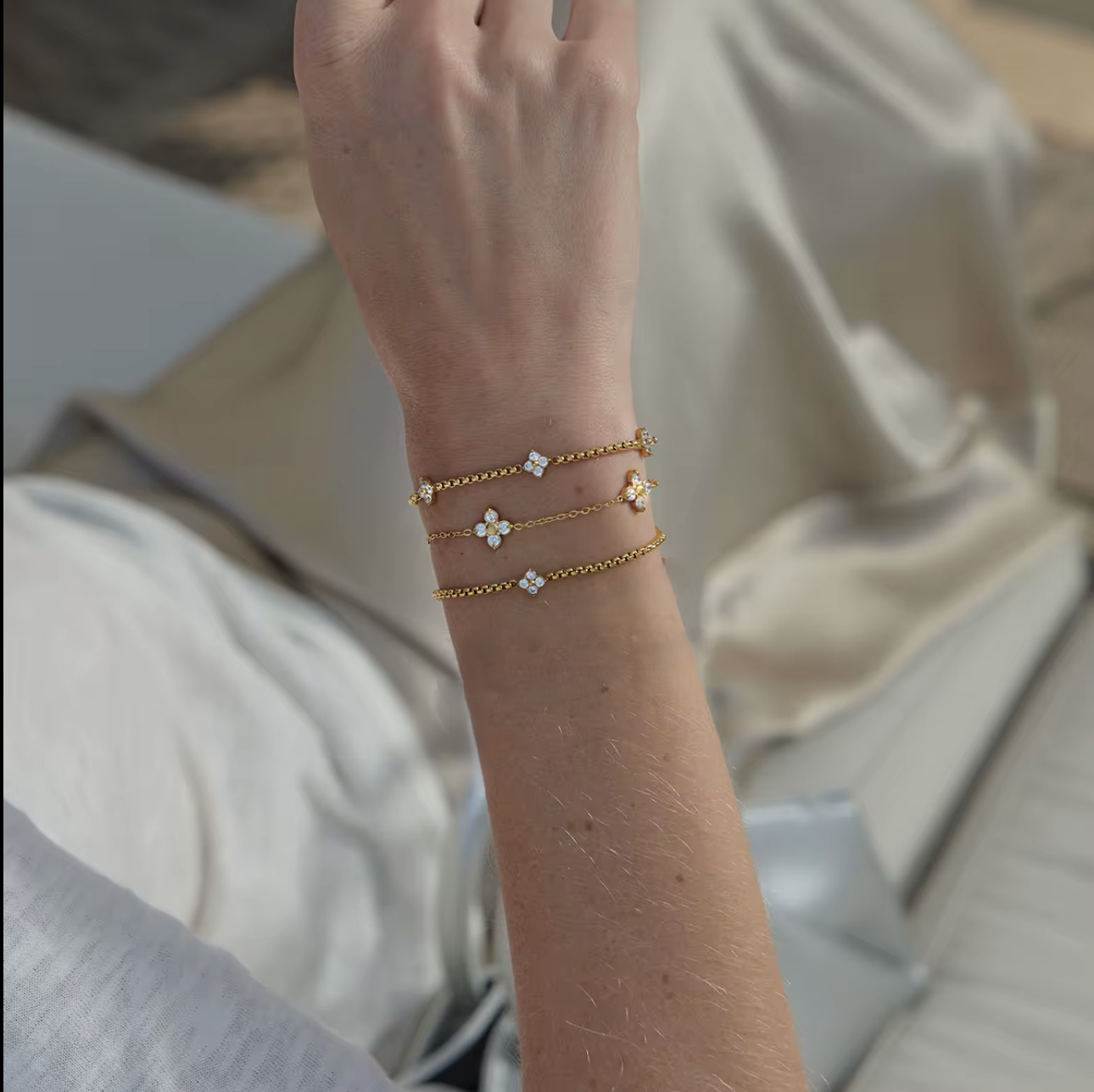 Close-up of a person's wrist wearing multiple gold bracelets with floral and heart designs.