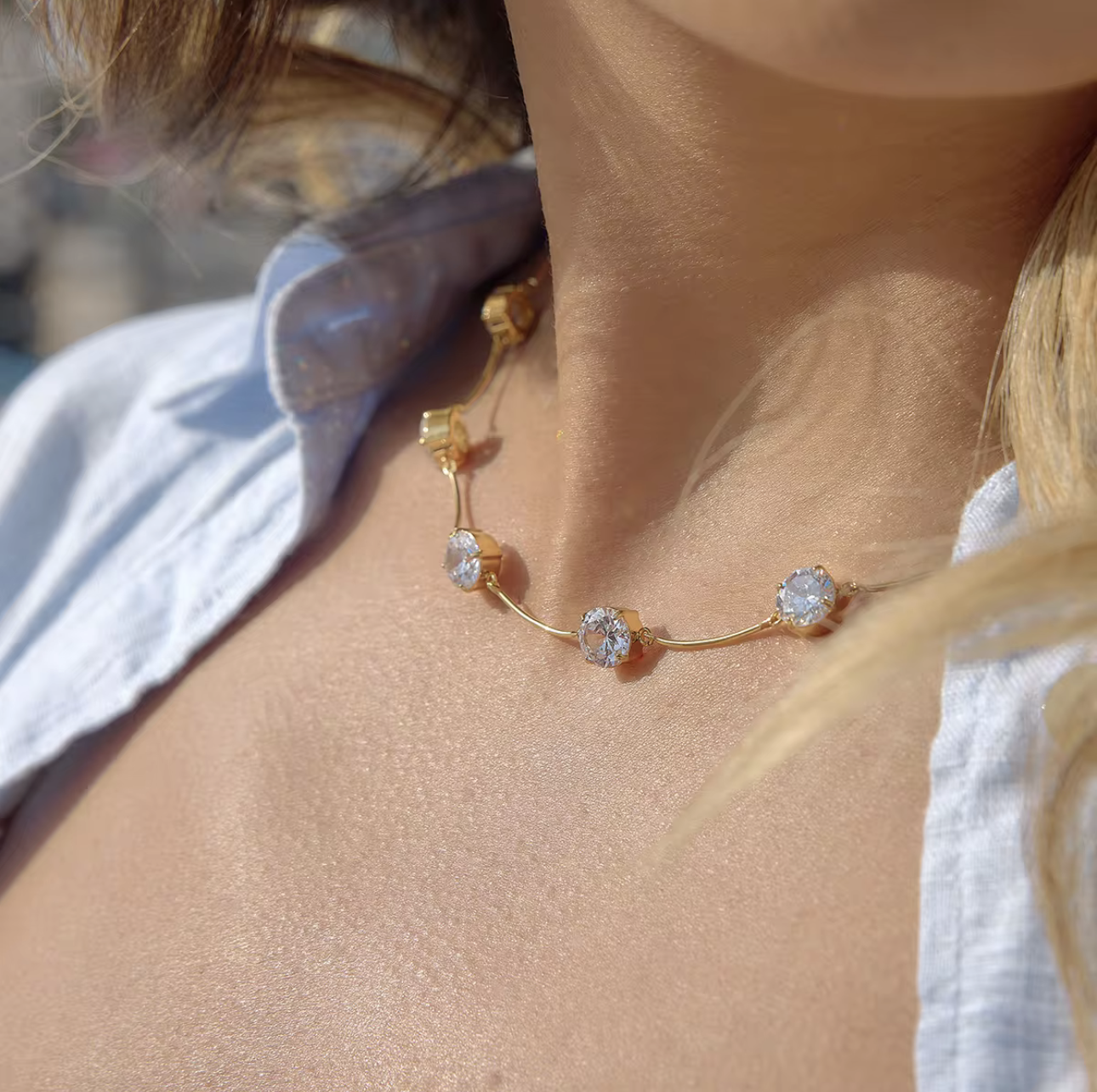 Close-up of a gold necklace with floral design on a person wearing a white top.